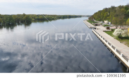 View of the dam and the river reflected in the blue sky with clouds. View from above. Beautiful landscape. White clouds reflected in the surface of the dark water. View of the dam and the river reflected in the blue sky with clouds. View from above. Beautiful landscape. White clouds reflected in the surface of the dark water. 109361395
