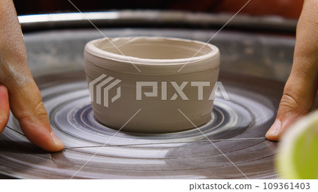 Women's fingers with thread for cutting a clay blank from the potter's wheel. Close-up. A master working in a pottery workshop. The concept of handwork, art and craft. 109361403