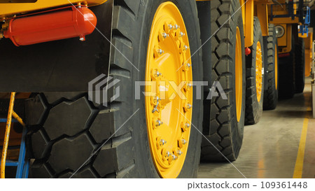 Assembly line of large dump trucks. Finished dump trucks stand in a row in the production shop. Close-up of the wheels of the car. Production of yellow quarry dump trucks. Assembly line of large dump trucks. Finished dump trucks stand in a row in the production shop. Close-up of the wheels of the car. Production of yellow quarry dump trucks. 109361448
