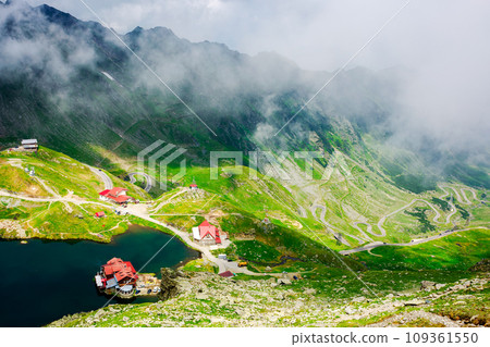 landscape of high altitude mountain lake in summer. nature scenery of valley with transfagarasan road in the distance beneath a sky with clouds on a sunny day. popular travel destination of romania landscape of high altitude mountain lake in summer. nature scenery of valley with transfagarasan road in the distance beneath a sky with clouds on a sunny day. popular travel destination of romania 109361550