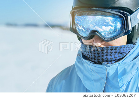 Close up of the ski goggles of a man with the reflection of snowed mountains.  A mountain range reflected in the ski mask.  Man  on the background blue sky. Wearing ski glasses. Winter Sports. 109362207
