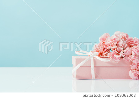 Pink gift box with tender pink carnation flowers. Blue background. Gift or holiday concept. Mothers Day, birthday wedding or St Valentines day with copy space. Minimal Pink gift box with tender pink carnation flowers. Blue background. Gift or holiday concept. Mothers Day, birthday wedding or St Valentines day with copy space. Minimal 109362308