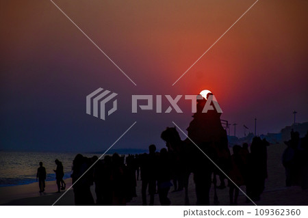 Silhouette of beach life Scene on a clear dusk with orange Sun behind a couple at renowned Indian seashore of Puri, Odisha, India,Asia. 12th February 2020. Silhouette of beach life Scene on a clear dusk with orange Sun behind a couple at renowned Indian seashore of Puri, Odisha, India,Asia. 12th February 2020. 109362360