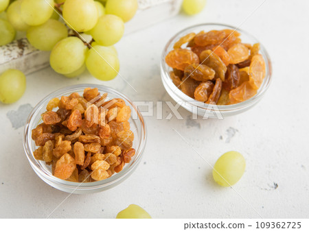 Sweet dried green raisins in glass bowl with ripe grapes in wooden box 109362725