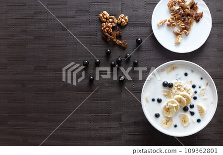 Healthy breakfast concept with oatmeal porridge with bananas, milk, blueberries,  nuts, raisins, chia seeds and currants. Top view. Super food 109362801