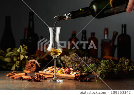 Yellow herbal liquor or balm is poured from a vintage bottle into a glass. Yellow herbal liquor or balm is poured from a vintage bottle into a glass. 109363342