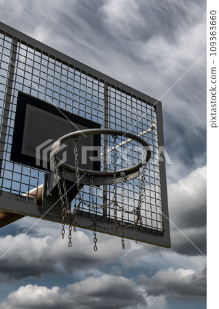 Metal Basketball Board And Ring With Chains In Front Of Sky With Heavy Clouds 109363660