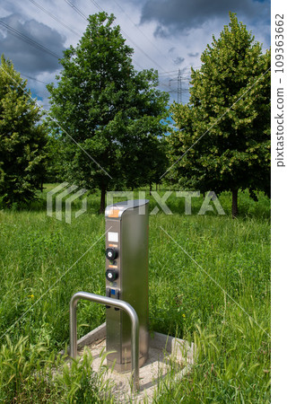 Charging Station For Electric Cars In Green Meadow In Front Of Trees And Electricity Cables Charging Station For Electric Cars In Green Meadow In Front Of Trees And Electricity Cables 109363662