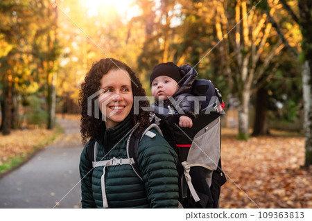 Mother walking in Suburban Neighborhood with Baby in Carrier. Fall Season Mother walking in Suburban Neighborhood with Baby in Carrier. Fall Season 109363813