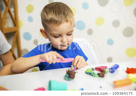 Little boy enthusiastically plays with plasticine, play dough on white table 109364175