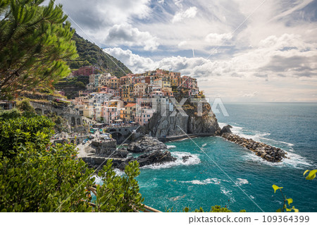 Stunning view of Manarola village in Cinque Terre National Park, beautiful cityscape with colorful houses and green terraces on cliffs over a sea, Liguria region of Italy. 109364399
