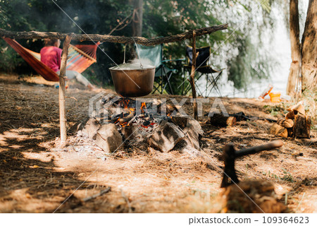 Travel a kettle over a fire burning on the river and sunset backgroun. Cooking over a campfire Travel a kettle over a fire burning on the river and sunset backgroun. Cooking over a campfire 109364623