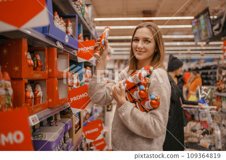 Stack of Chocolate Santa Clauses. Christmas time. A young woman chooses a gift set for Christmas to a child on a supermarket shelf. Stack of Chocolate Santa Clauses. Christmas time. A young woman chooses a gift set for Christmas to a child on a supermarket shelf. 109364819