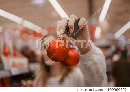Cute young woman choosing artificial Christmas tree in Xmas store. Christmas concept store, buying ornaments. A woman buys New Year's decorations for a Christmas tree in a store. 109364852