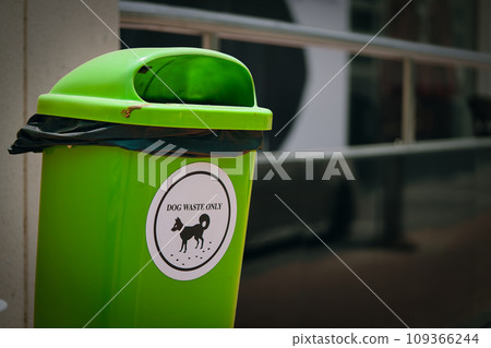 Environmentally conscious solution, this green trash bin with a white sticker to dog waste disposal, highlighting ecological mindfulness and the importance of cleaning up after dogs. Environmentally conscious solution, this green trash bin with a white sticker to dog waste disposal, highlighting ecological mindfulness and the importance of cleaning up after dogs. 109366244