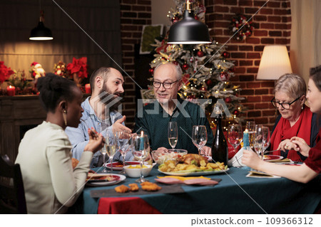 Happy family on christmas eve holiday, gathering to celebrate festive dinner together and drink alcohol, december season. Young and senior people feeling jolly around the table with food and wine. 109366312