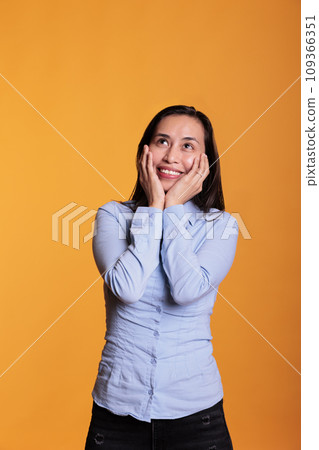 Positive filipino woman smiling in front of studio camera, posing with joyful expressions over yellow background. Confident cheerful model feeling excited and happy enjoying good times 109366351