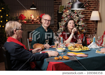 Old person at table on xmas with family eating traditional meal and celebrating christmas holiday at home. Senior people hosting festive xmas dinner event during winter season. 109366358
