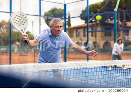 Aged man playing paddleball match on outdoor court 109366934