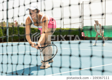 Pretty woman holding tennis racket and looking concentrated while standing on tennis court. Pretty woman holding tennis racket and looking concentrated while standing on tennis court. 109367111