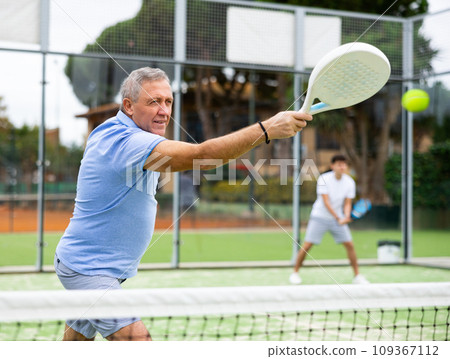 View through the tennis net at an elderly player in game of padel View through the tennis net at an elderly player in game of padel 109367112