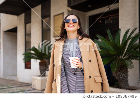 Happy smiling woman in sunglasses and coat walks Happy smiling woman in sunglasses and coat walks 109367499