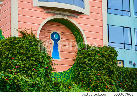 Abstract colorful magical keyhole in side of building surrounded by green hedges 109367605