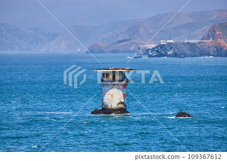 Abandoned lighthouse structure in middle of bay with distant mountainous coastline 109367612