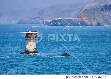 Abandoned lighthouse structure in middle of bay with distant mountainous coast 109367616