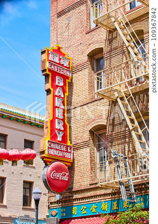 Large sign for bakery on side of tan brick building with light yellow fire escape ladders 109367842