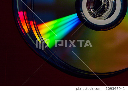 Stacked CDs in dark setting with cone of rainbow colored light shaft across silvery surface 109367941