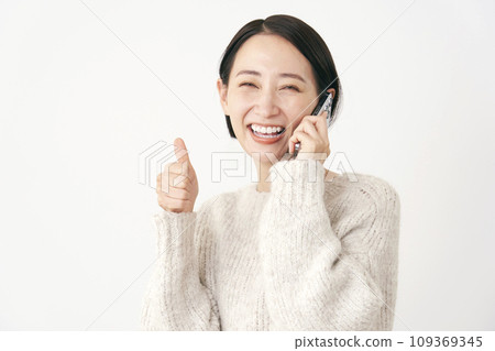 Middle-aged woman giving a good sign while calling on a smartphone, white background Middle-aged woman giving a good sign while calling on a smartphone, white background 109369345