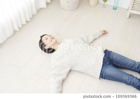 A woman lying on her back on the wooden floor in the living room 109369366