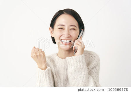 A middle-aged woman doing a fist pump while talking on a smartphone, white background A middle-aged woman doing a fist pump while talking on a smartphone, white background 109369378