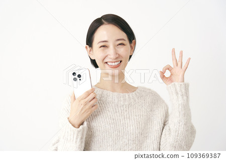 拿著智慧型手機並給予 OK 手勢的中年婦女，白色背景 109369387
