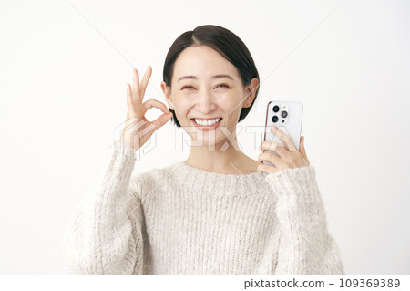 拿著智慧型手機並給予 OK 手勢的中年婦女，白色背景 109369389