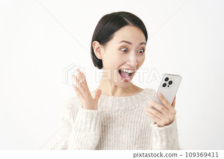 A middle-aged woman looking at her smartphone and smiling, surprised, white background A middle-aged woman looking at her smartphone and smiling, surprised, white background 109369411