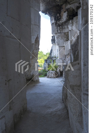 A rectangular opening in a dark, mossy limestone cave frames a bright blue sky with fluffy white clouds in Setigi, Gresik, East Java, Indonesia. A rectangular opening in a dark, mossy limestone cave frames a bright blue sky with fluffy white clouds in Setigi, Gresik, East Java, Indonesia. 109370142