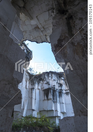 A rectangular opening in a dark, mossy limestone cave frames a bright blue sky with fluffy white clouds in Setigi, Gresik, East Java, Indonesia. A rectangular opening in a dark, mossy limestone cave frames a bright blue sky with fluffy white clouds in Setigi, Gresik, East Java, Indonesia. 109370143