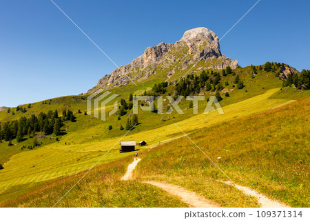 View of Peitlerkofel with wooden houses, green trees and grand mountain View of Peitlerkofel with wooden houses, green trees and grand mountain 109371314