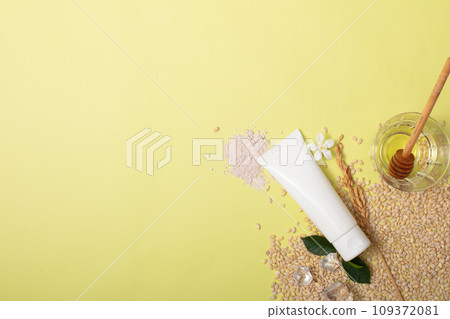 An unlabeled tube of rice bran extract facial cleanser is displayed against a background of whole rice grains. Ideal space for advertising vegan cosmetics. An unlabeled tube of rice bran extract facial cleanser is displayed against a background of whole rice grains. Ideal space for advertising vegan cosmetics. 109372081