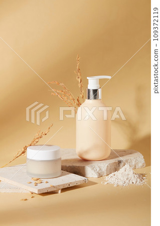 Front view of a jar of lotion and a bottle of shower gel are placed on a podium with rice bran powder on a beige background. Skin care with natural ingredients. Front view of a jar of lotion and a bottle of shower gel are placed on a podium with rice bran powder on a beige background. Skin care with natural ingredients. 109372119