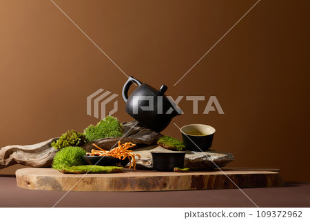 A black tea set arranged on a wooden platform, accompanied by green moss and cordyceps. Harness the benefits of cordyceps tea for combating fatigue, cough, and post-illness weakness. A black tea set arranged on a wooden platform, accompanied by green moss and cordyceps. Harness the benefits of cordyceps tea for combating fatigue, cough, and post-illness weakness. 109372962