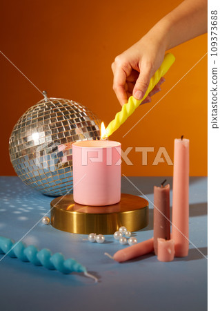 Close up of woman hand lighting candles on colorful background. Candles, pearls and a disco ball decorated on the table. Party atmosphere. Creative space for ads. 109373688