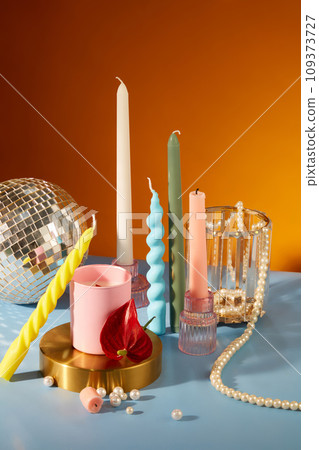 Colorful candles are displayed on a table with a string of pearls, a glass and a disco ball. The colorful space is suitable for birthdays and holidays. 109373727