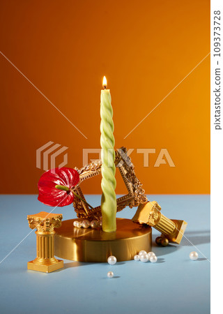 Front view of a burning candle displayed with vintage props on a blue-orange background. Copy space for birthdays or holidays. Uses of candles. 109373728