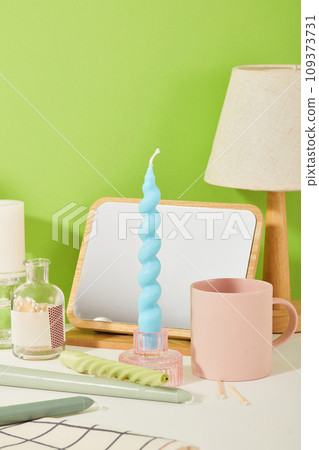 A blue candle is inserted into a glass candlestick. On the table there are many utensils such as mirror, ceramic cup, lamp, etc. Delicate images suitable for many themes. 109373731