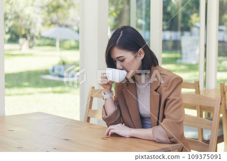 Asian Woman drink black coffee hand holding cup at green garden cafe. Young woman smile face love drink coffee. Beauty woman drinking black coffee in coffee shop holding freshness cup. Coffee lover Asian Woman drink black coffee hand holding cup at green garden cafe. Young woman smile face love drink coffee. Beauty woman drinking black coffee in coffee shop holding freshness cup. Coffee lover 109375091