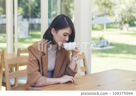 Asian Woman drink black coffee hand holding cup at green garden cafe. Young woman smile face love drink coffee. Beauty woman drinking black coffee in coffee shop holding freshness cup. Coffee lover 109375094