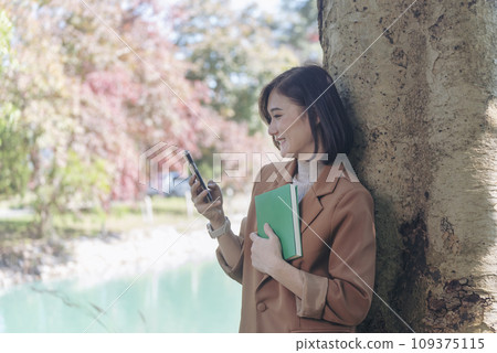 Happy asian woman reading book outdoor in green park nature. Reading book magazine relaxation woman. Leisure portrait woman smile sitting in green park read e-book diary planner with happy face Happy asian woman reading book outdoor in green park nature. Reading book magazine relaxation woman. Leisure portrait woman smile sitting in green park read e-book diary planner with happy face 109375115